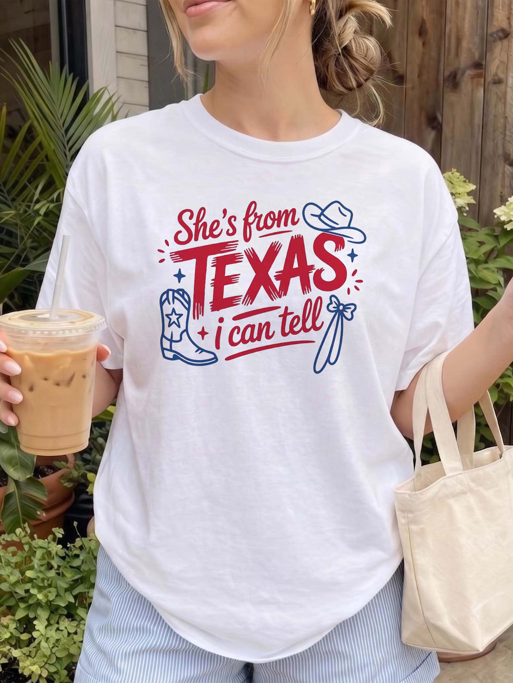 A white graphic t-shirt with a red and blue Texas cowboy design, worn by a woman holding an iced drink.
