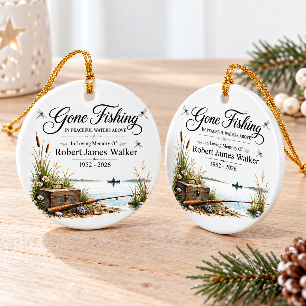 Two round ceramic memorial fishing ornaments displayed on a wooden surface with a gold cord