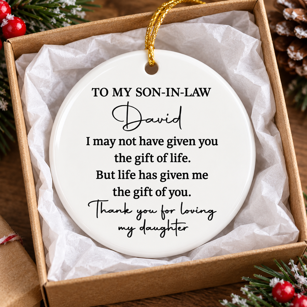 Ceramic Christmas ornament for son in law resting inside an open gift box lined with white tissue paper.