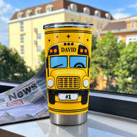 Stainless steel school bus driver tumbler placed on a windowsill with a blurred yellow building and newspaper in the
