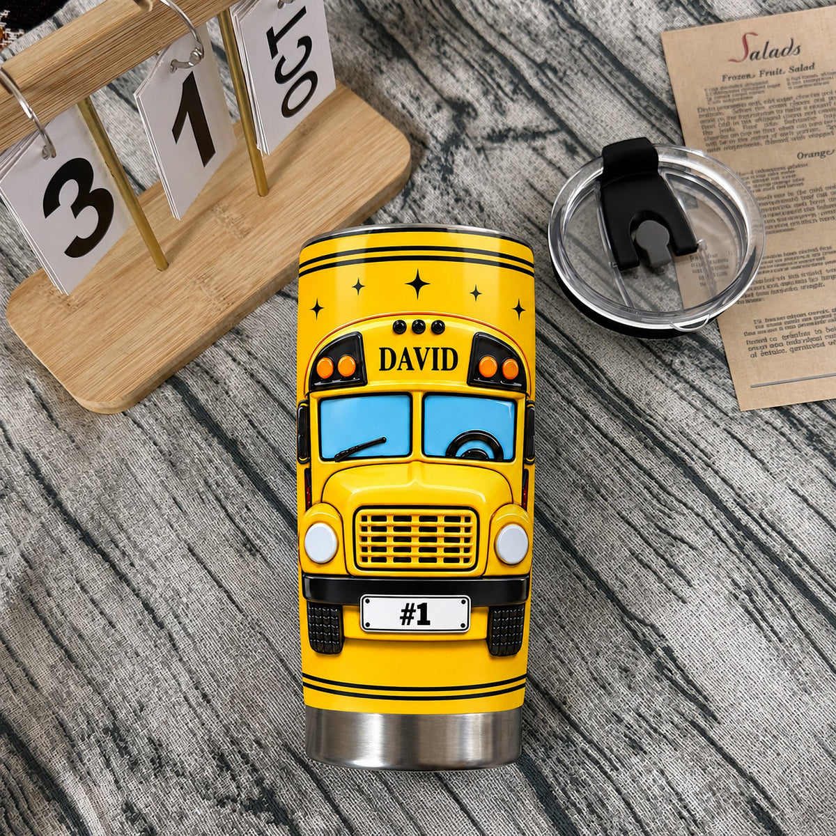 School bus driver tumbler stainless steel travel cup with custom David name on a wooden tabletop next to its lid.