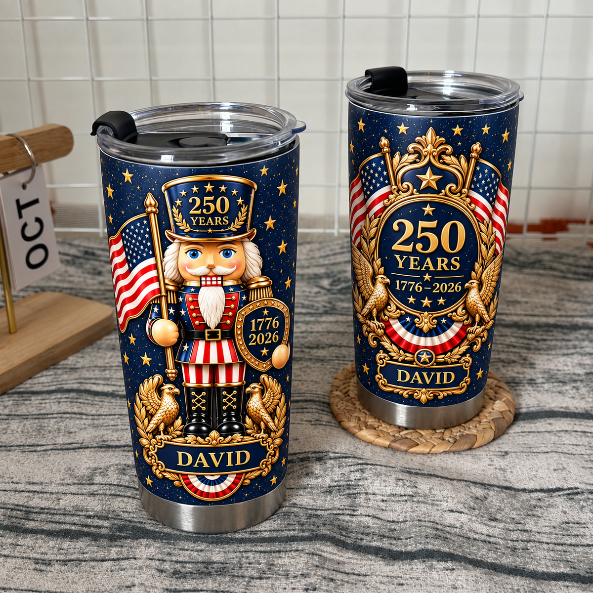 Two stainless steel travel mugs with historical design standing on a woven coaster against a wire grid wall.