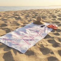 White beach towel with pink future mrs text laid on sand with straw hat, sunglasses, and coral flip flops.