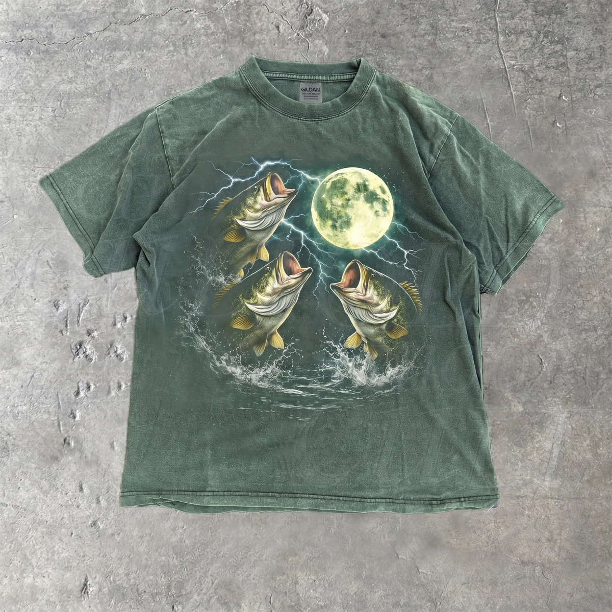 A garment-dyed forest green T-shirt laid flat shows a vintage fishing graphic with bass, lightning, and a bright moon.