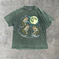 A garment-dyed forest green T-shirt laid flat shows a vintage fishing graphic with bass, lightning, and a bright moon.