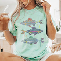 A pale green oversized t-shirt featuring denim fish graphics, worn by a woman holding an iced coffee.