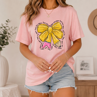 A woman in a light pink t-shirt with a yellow bow and pencil print, styled with denim shorts.
