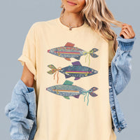 A person wearing a light yellow oversized graphic t-shirt featuring three denim fish with colorful bows, layered under a
