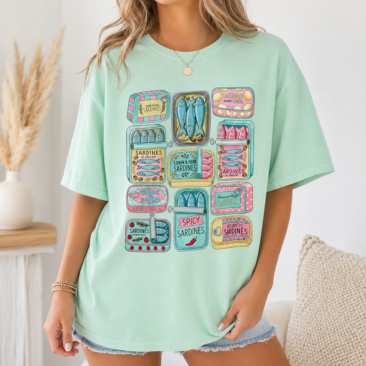 A woman in a mint green oversized graphic t-shirt displaying a colorful sardine can design.