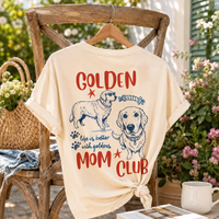 Cream colored graphic t-shirt draped on wooden chair with tote bag, floral background and coffee cup.