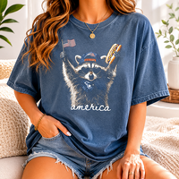 A vintage blue t-shirt featuring a raccoon wearing a cap and holding a hot dog and flag.