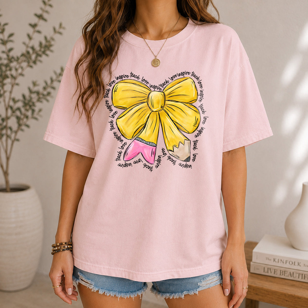 A woman in a pastel pink t-shirt with a yellow bow and pencil design, styled with denim shorts.