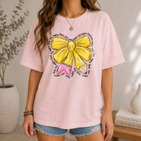 A woman in a pastel pink t-shirt with a yellow bow and pencil design, styled with denim shorts.