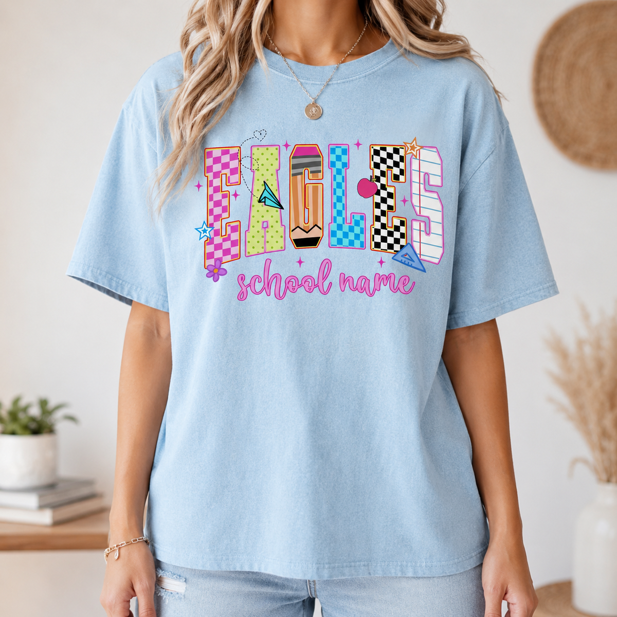A woman modeling a light blue t-shirt with a colorful school spirit graphic.