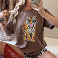 A woman sitting on a white surface, wearing a brown oversized T-shirt with a tiger graphic.