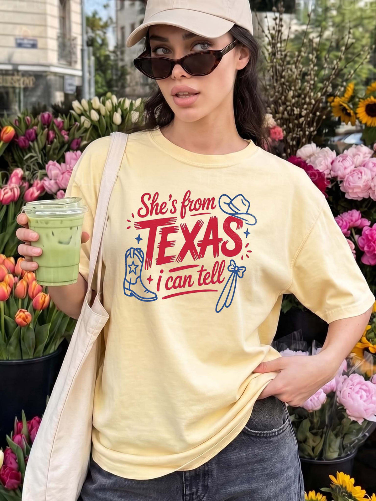 A light yellow graphic t-shirt featuring a western Texas design, displayed on a woman near flowers.