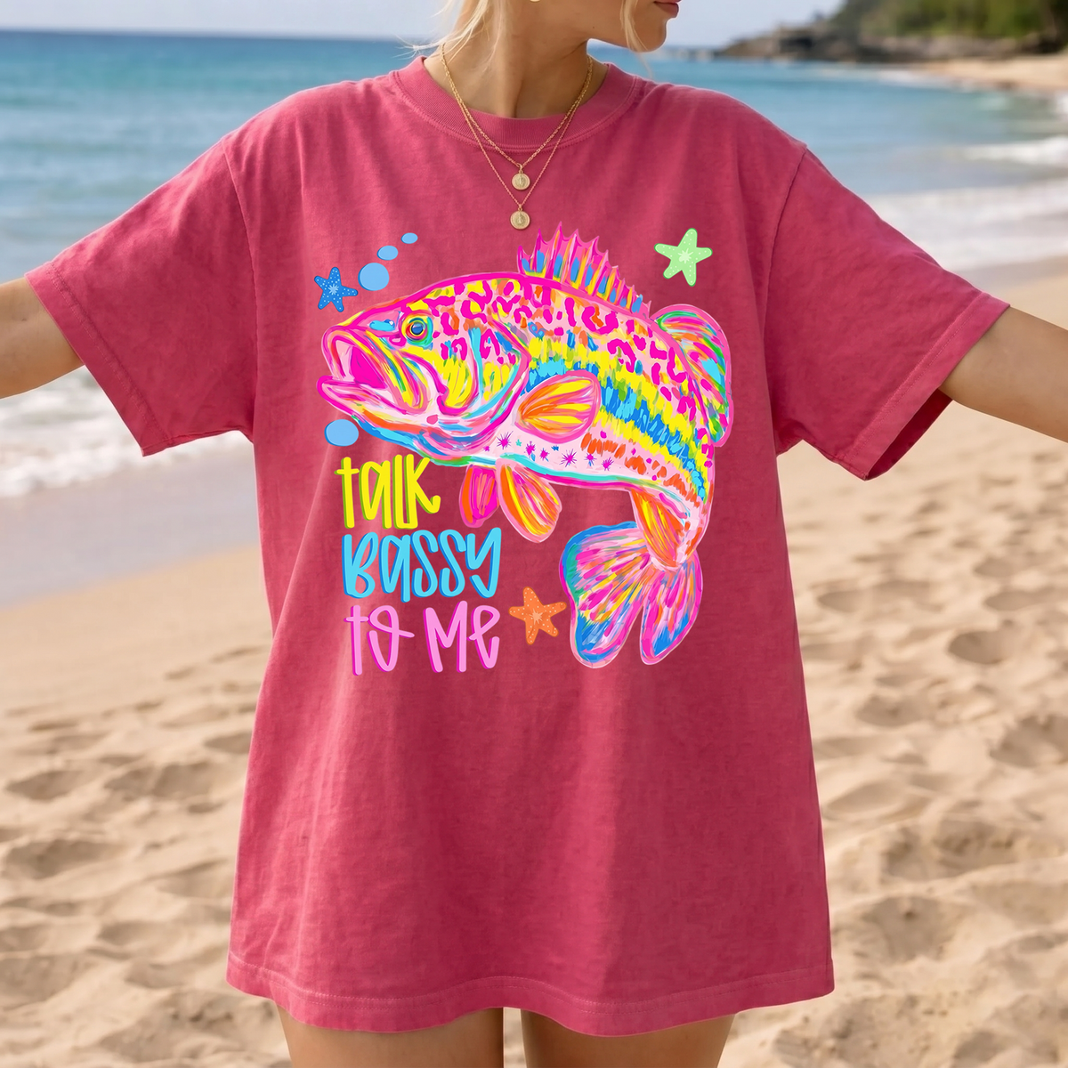 A woman modeling a red graphic t-shirt featuring a vibrant bass fish design by the ocean.