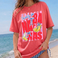 Coral pink women's t-shirt with retro banana graphic and blue striped bikini at the beach.
