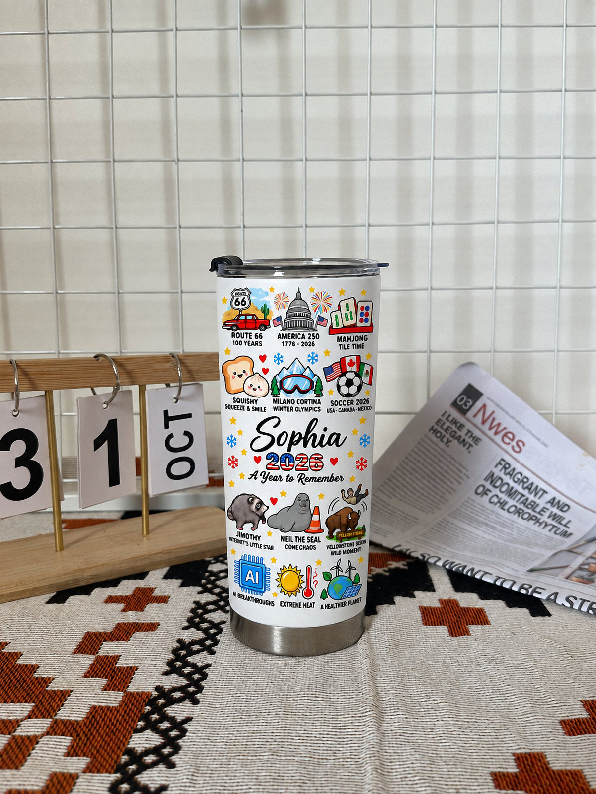 A Year to Remember Tumbler on a patterned mat beside a calendar and newspaper.