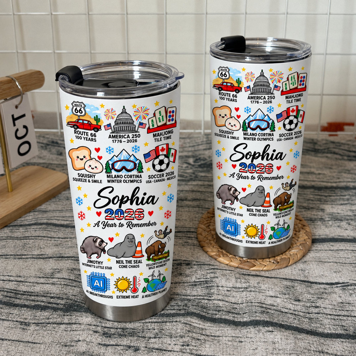 Two 2026 commemorative cups with black lids standing on a textured surface.