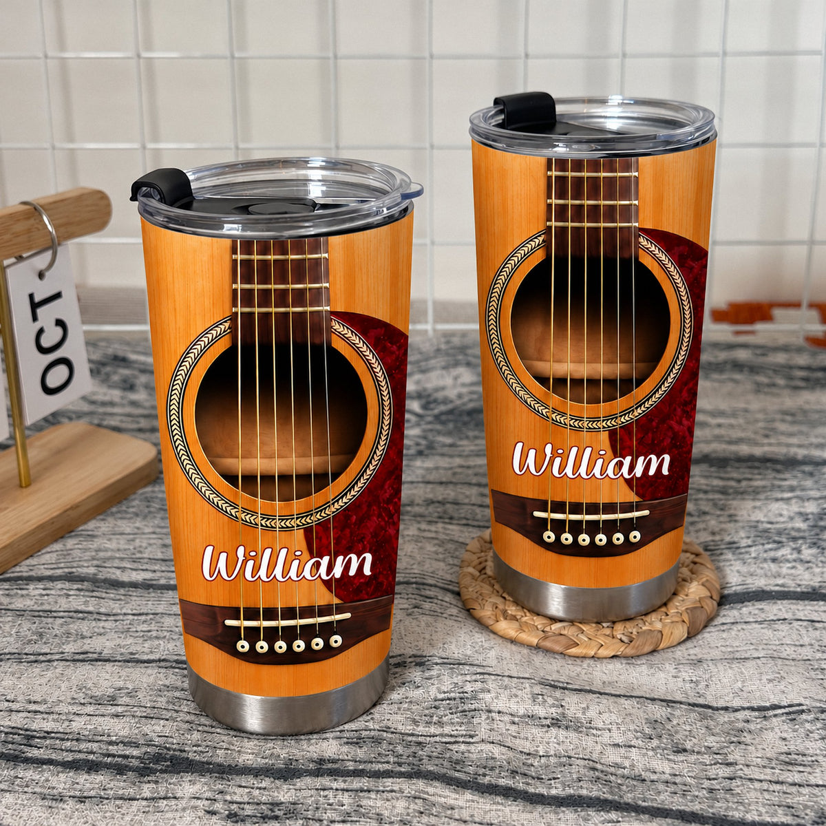 Two custom guitar stainless steel tumblers standing on a textured grey tabletop against a white grid wall.