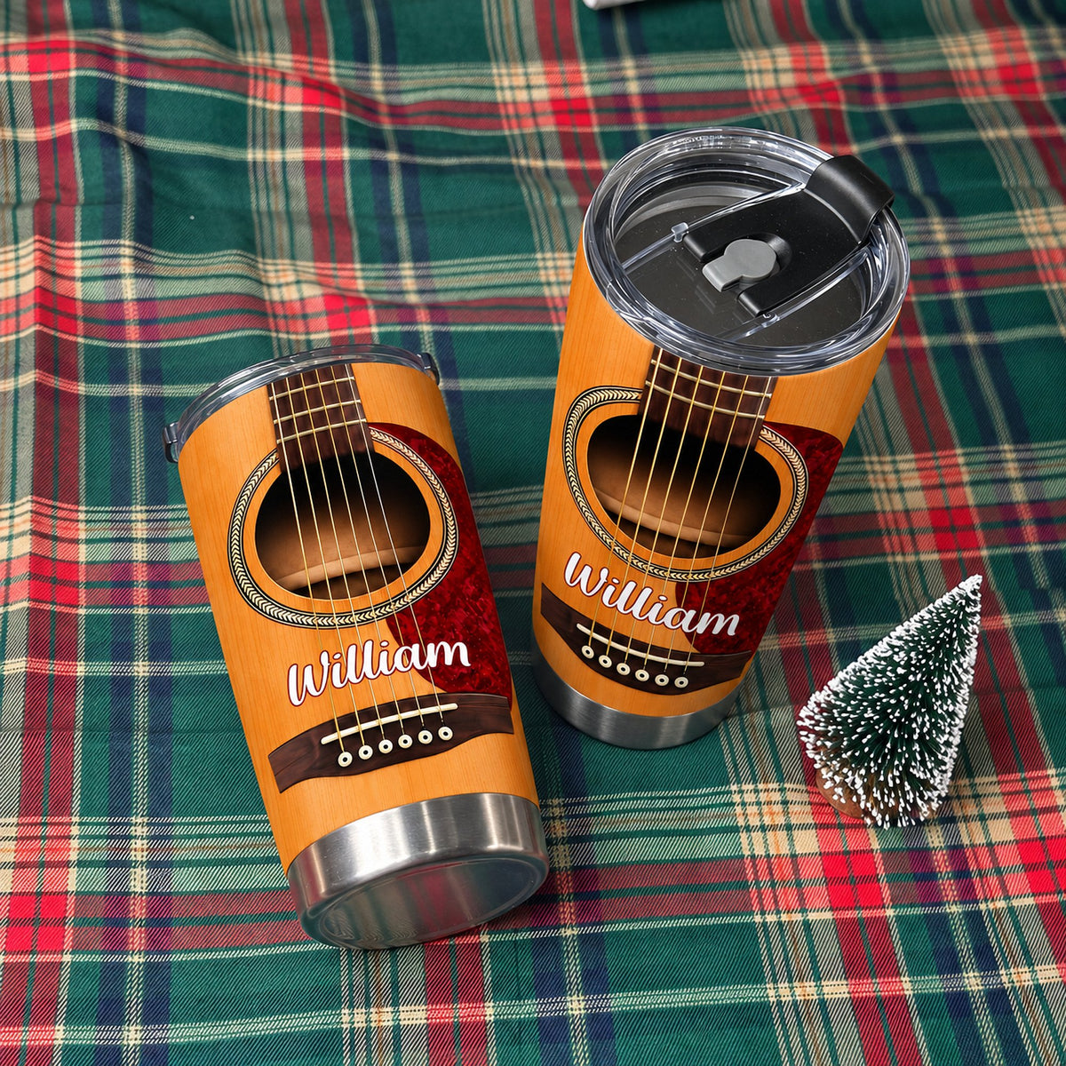 Personalized acoustic guitar travel mug and tumbler with lid resting on a green and red plaid blanket with mini tree.