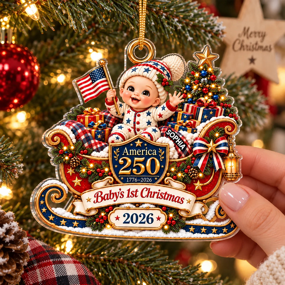 Close-up of a hand holding the personalized America 250 baby's first Christmas acrylic ornament with a cute sleigh design.