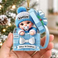 Hand holding a personalized blue number one acrylic ornament featuring a baby in a gift box with the name Ramson.