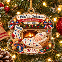 Close-up of a Baby's First Christmas acrylic ornament showing a sleeping baby in a basket, stocking, teddy bear, and 2026.