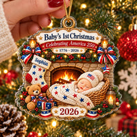Hand holding a Baby's First Christmas ornament with a patriotic America 250 theme, hanging on a decorated tree branch.