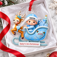A blue custom baby's first Christmas ornament rests inside a white gift box with red ribbon.