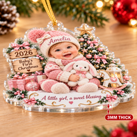 Detail view of the baby girl personalized acrylic ornament featuring pink knit hat and bunny toy on wood table.