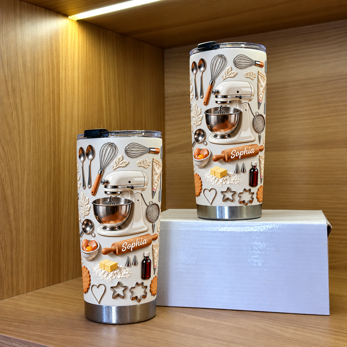 Two cream-colored insulated stainless steel tumblers with embossed baking theme displayed on a wooden shelf.
