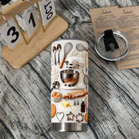 A custom name tumbler featuring an embossed mixer and rolling pin next to a wooden desk calendar and lid.