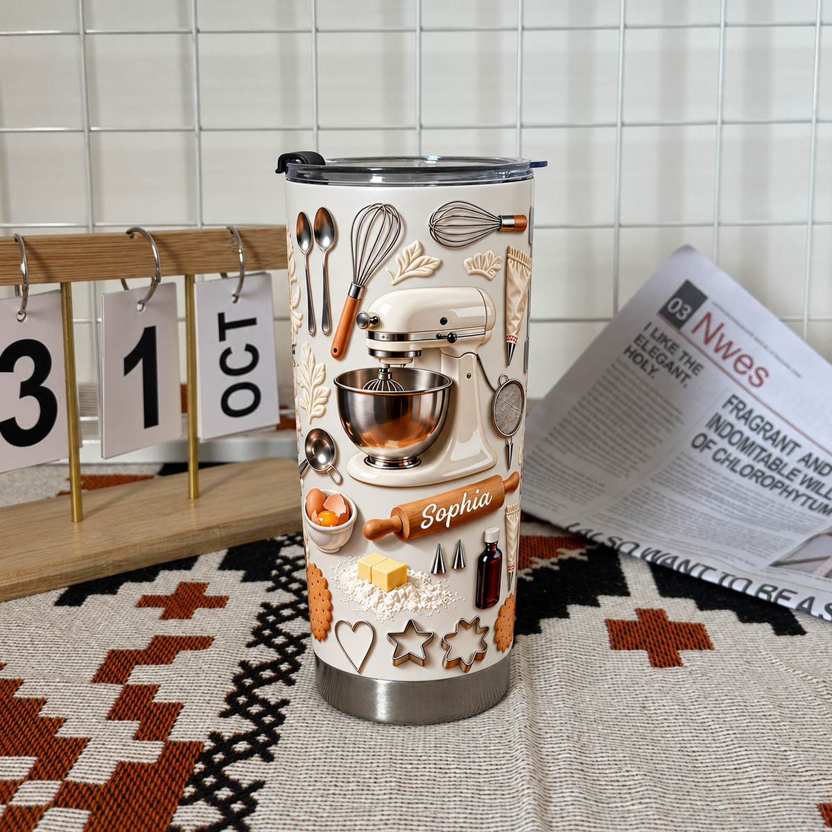 Insulated baking-themed tumbler with 3D embossed mixer design standing next to a calendar and newspaper.