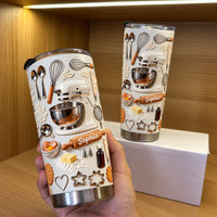Two personalized baker gift tumblers in cream with 3D stand mixer design held in a hand against a wooden shelf.