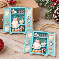 Two custom name baking ornaments displayed together on a rustic wooden surface next to pine branches and a gift.