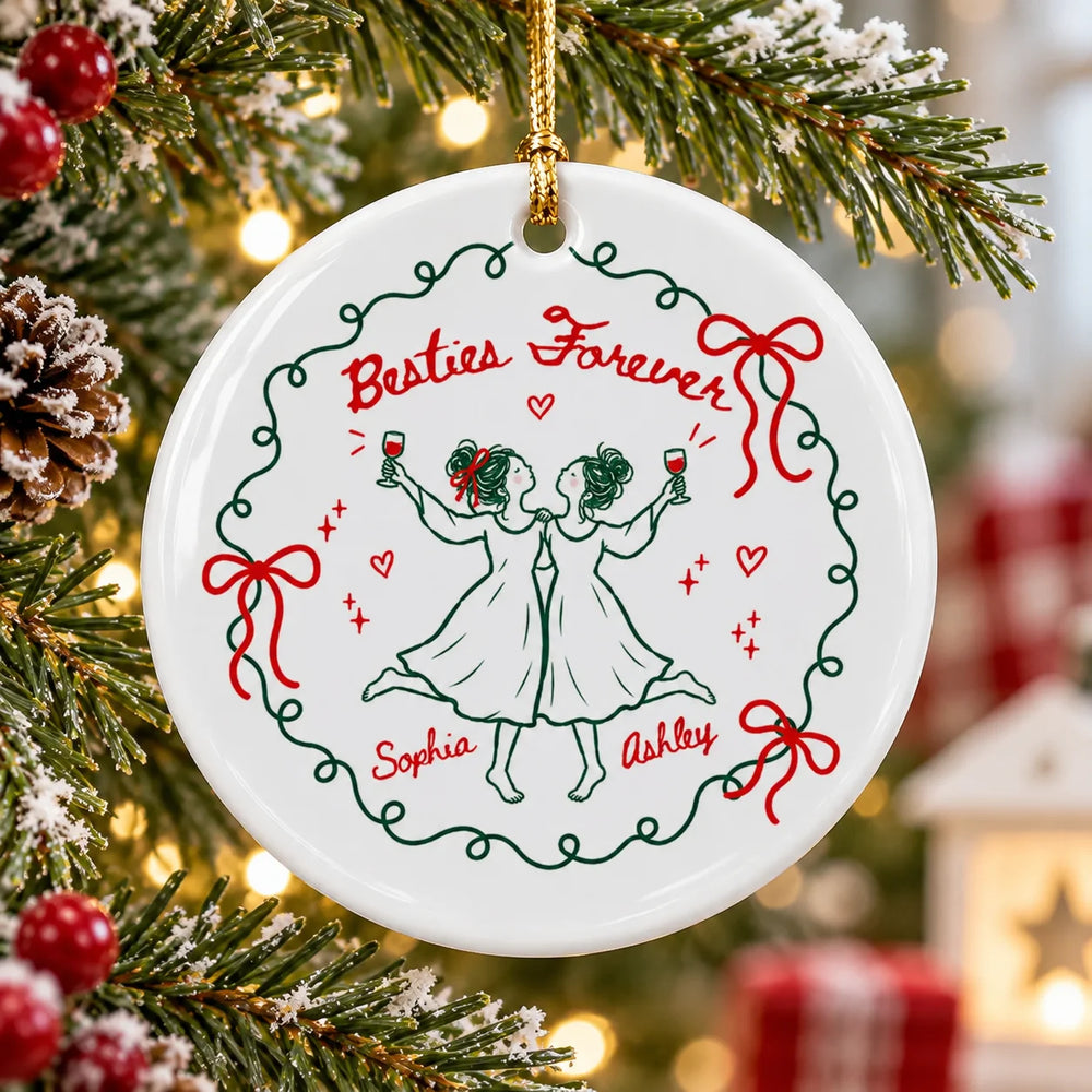 A single round ceramic Christmas ornament hanging on a pine tree with Besties Forever text, green wreath, and custom names