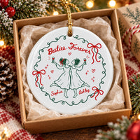 A round ceramic Christmas ornament resting inside a gift box lined with tissue paper under Christmas tree lights.