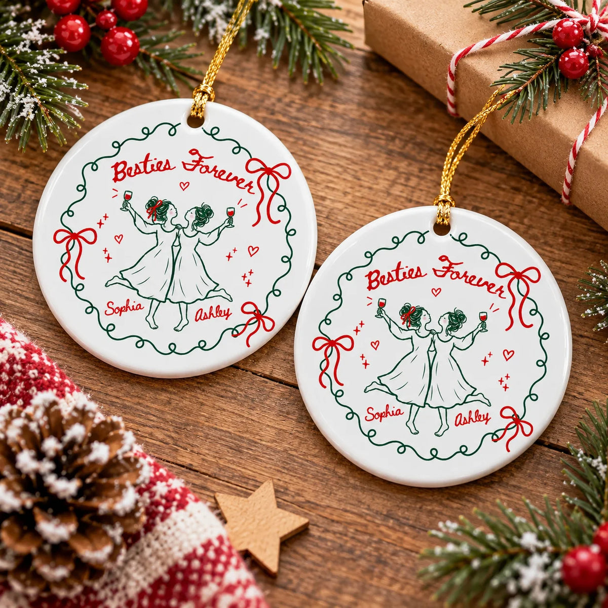 Two round ceramic Christmas ornaments laid out on a wooden table with pinecones and gift boxes nearby.