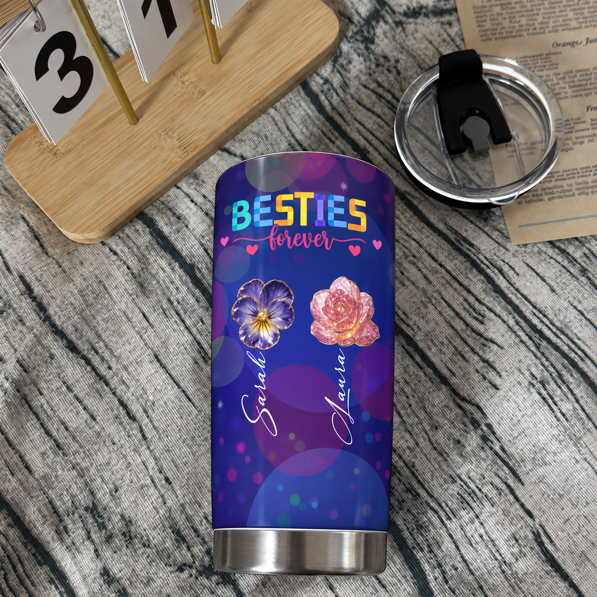 Best friend insulated tumbler with purple galaxy background and custom flowers resting on a wooden surface next to calendar