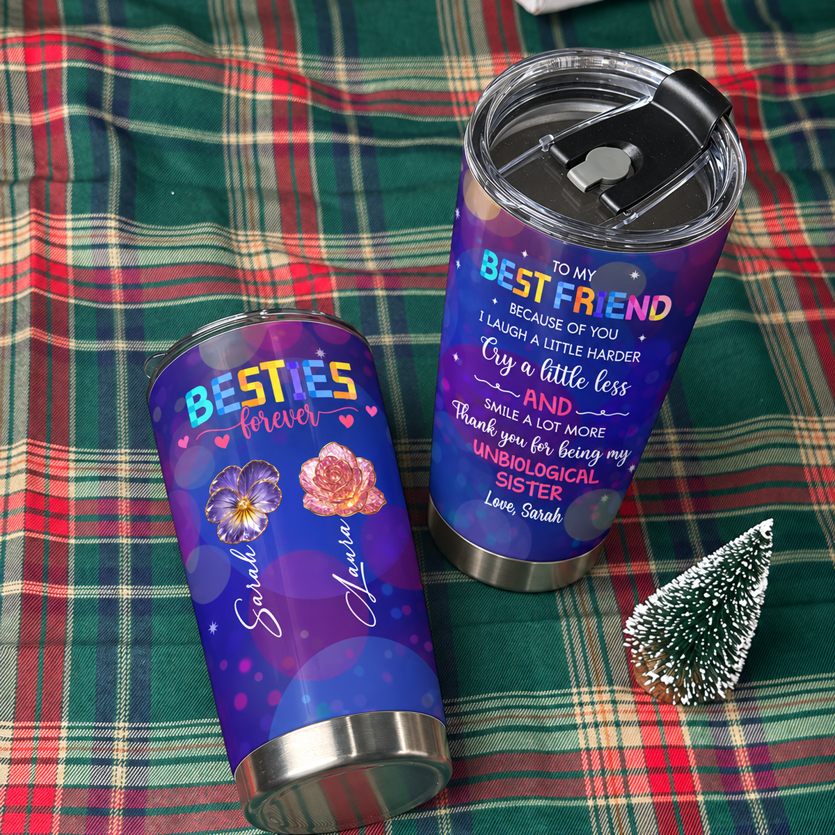 Two best friend insulated tumblers on a green plaid blanket next to a small decorative Christmas tree