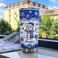 Blue glitter snowman tumbler on a marble windowsill with newspaper backdrop.