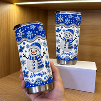 Hand holding blue glitter snowman tumbler next to another on box, wooden shelf.