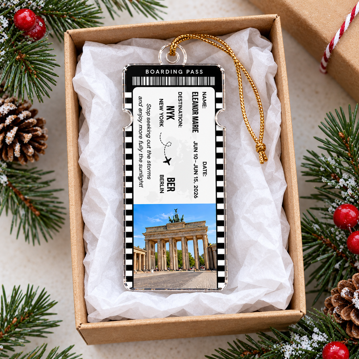 A plane ticket design acrylic ornament with Berlin destination details inside an open gift box on pine needles.