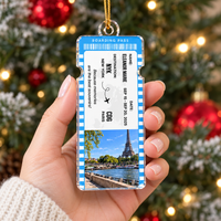 A person holding a blue vacation keepsake ornament with a plane ticket design in front of a Christmas tree.