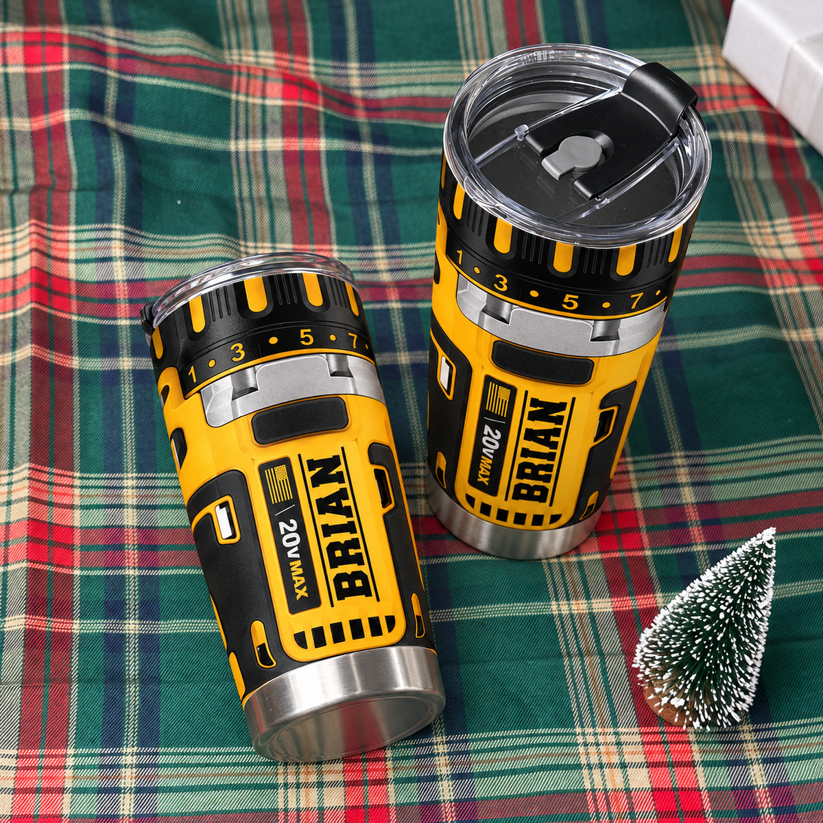 Two drill theme stainless steel insulated cups with name BRIAN resting on a green plaid blanket next to a mini Christmas
