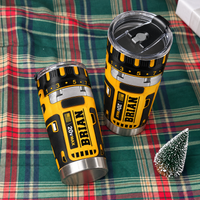 Two drill theme stainless steel insulated cups with name BRIAN resting on a green plaid blanket next to a mini Christmas