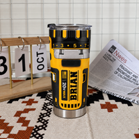 Drill theme stainless steel insulated cup with name BRIAN placed on a patterned rug next to a desk calendar and newspaper.