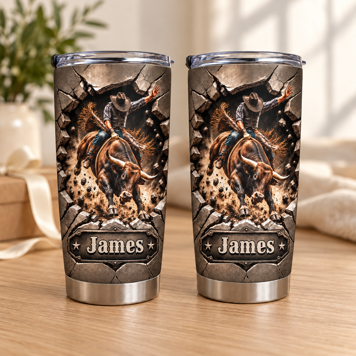 Two stainless steel cowboy tumblers featuring a customized nameplate and dynamic bull rider graphics on a wooden tabletop.